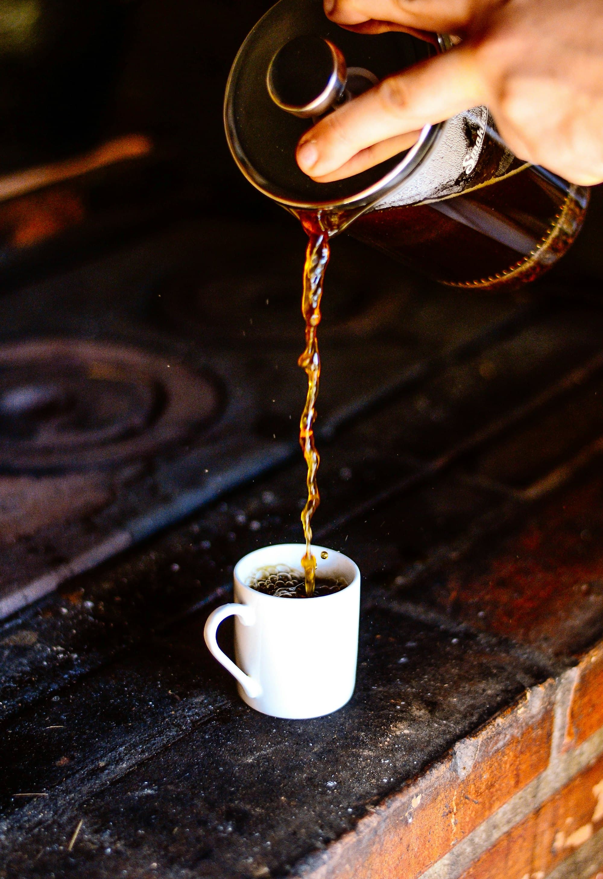 person pouring coffee from a french press on white ceramic teacup