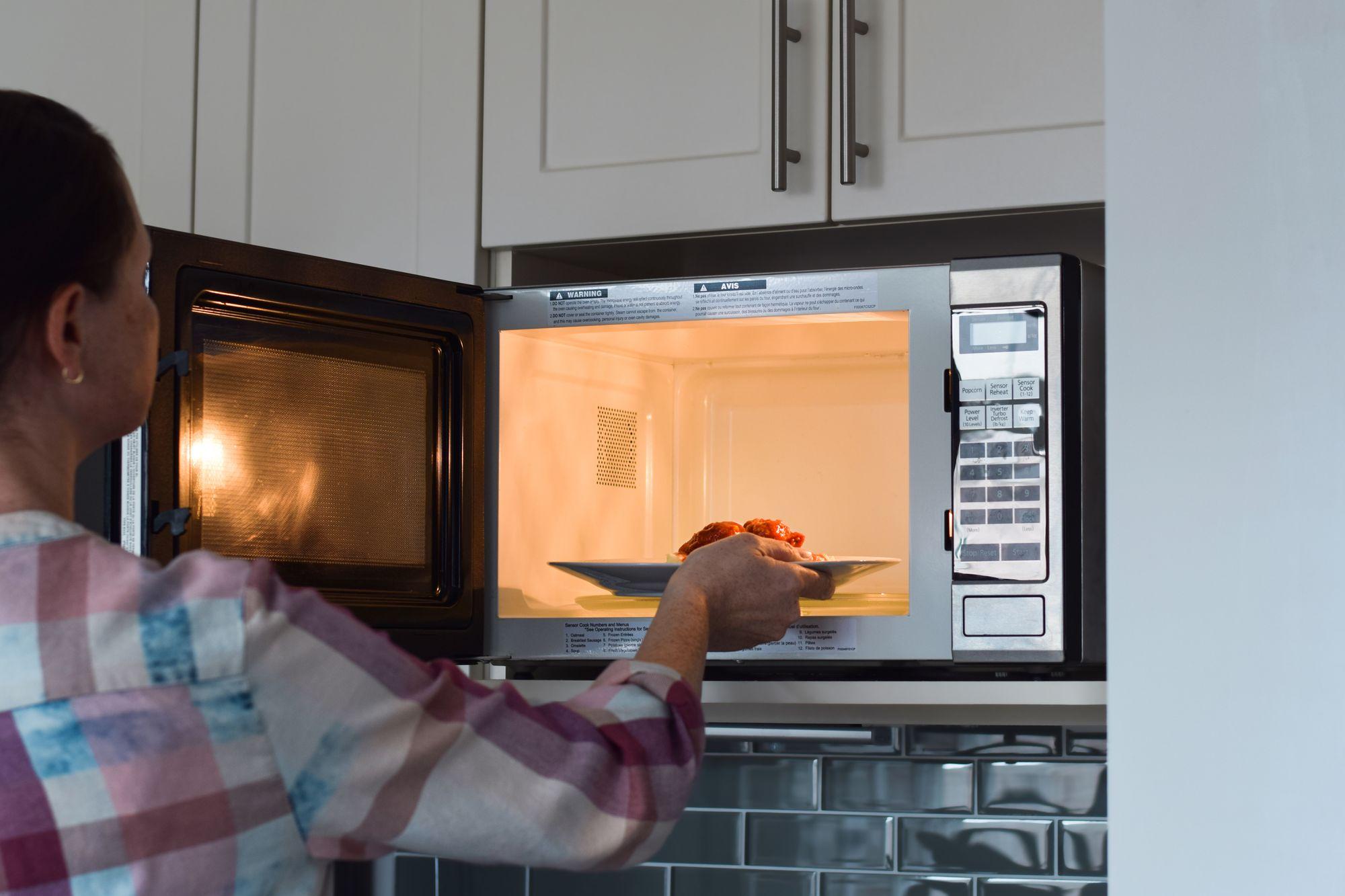 Image of a person placing a plate of food into the microwave.