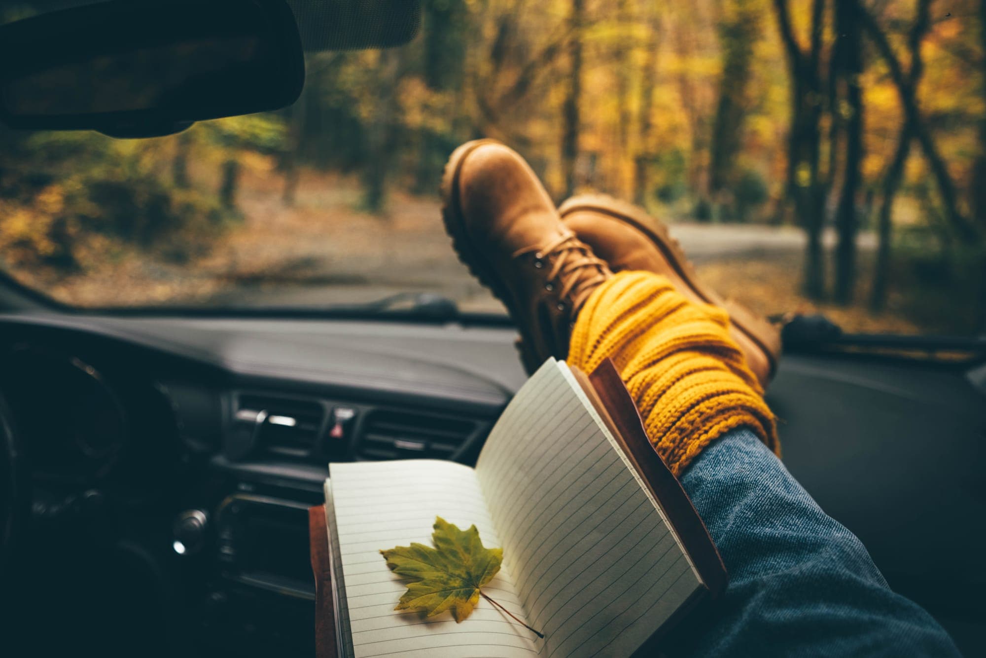 person with boots up on the dashboard holding a notebook