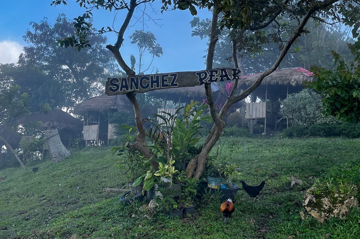 Sign that reads 'Sanchez Peak' with some huts behind it.