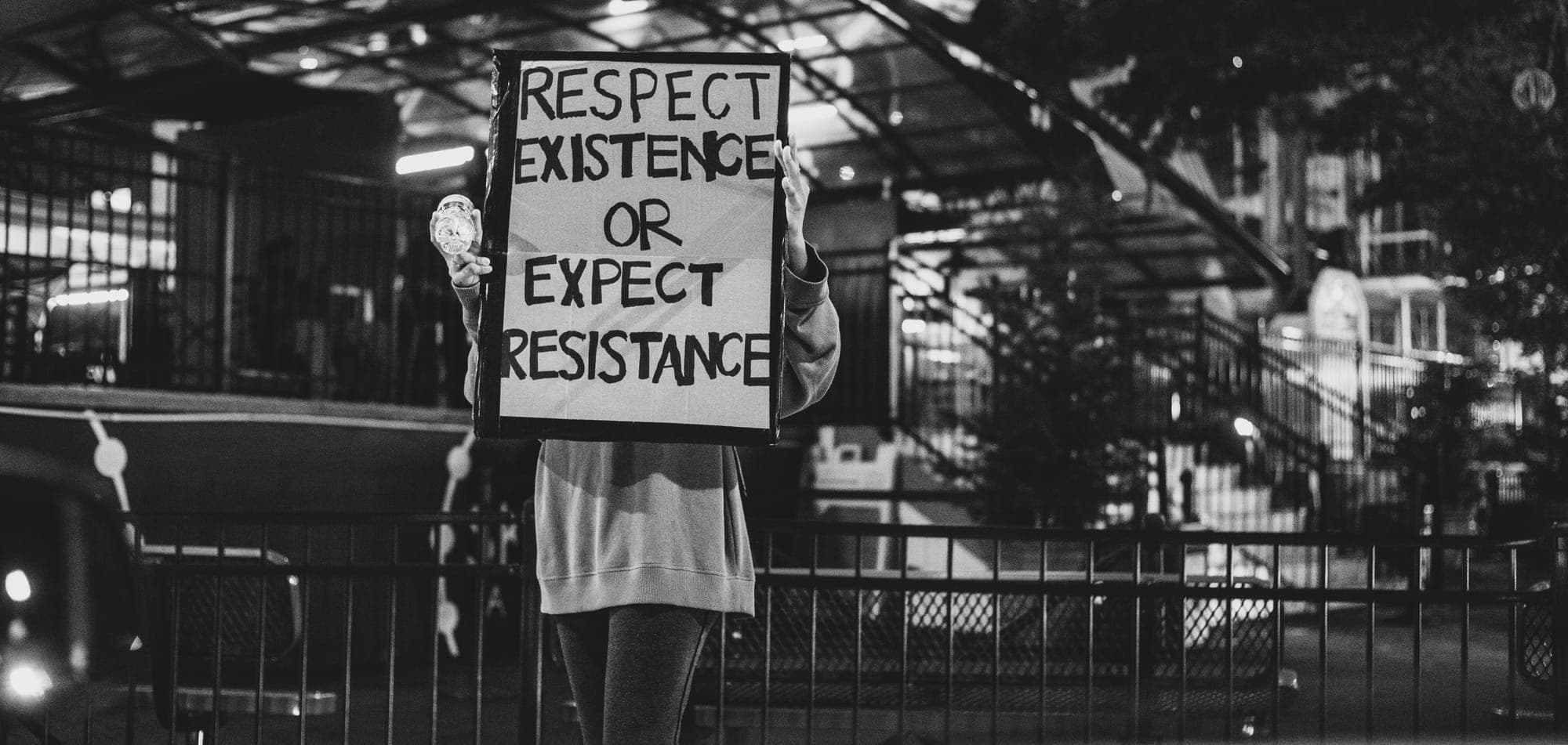 Grayscale image of a woman holding a sign that reads respect existence or expect resistance