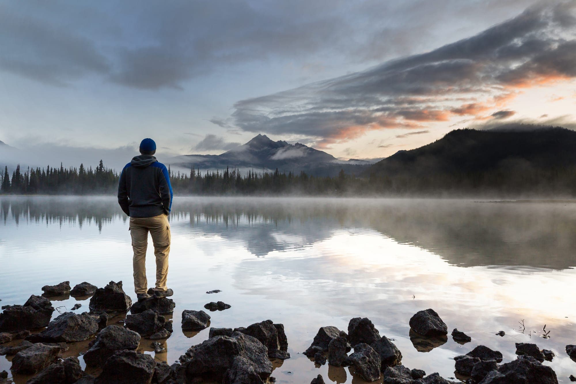 Man in hoody standing in front of a misty lake in the forest