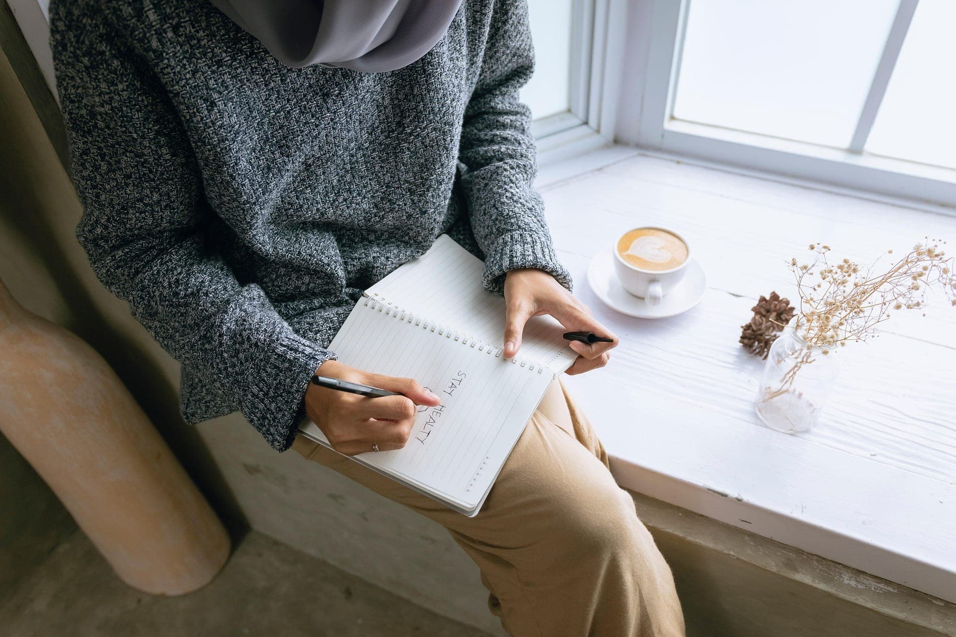 Person by a window with a journal that says 'stay healthy'